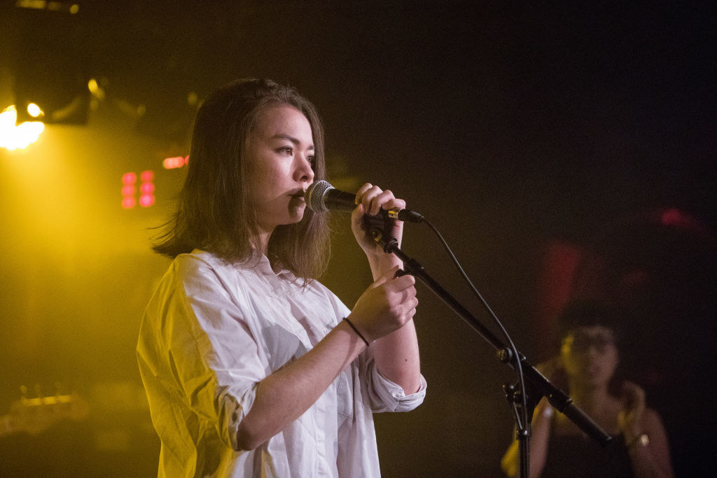 a woman wearing a button down shirt sings into a microphone