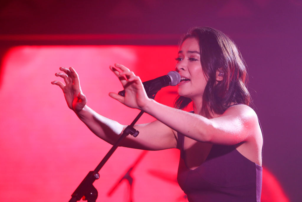 a woman outstretches her arms while singing into a microphone