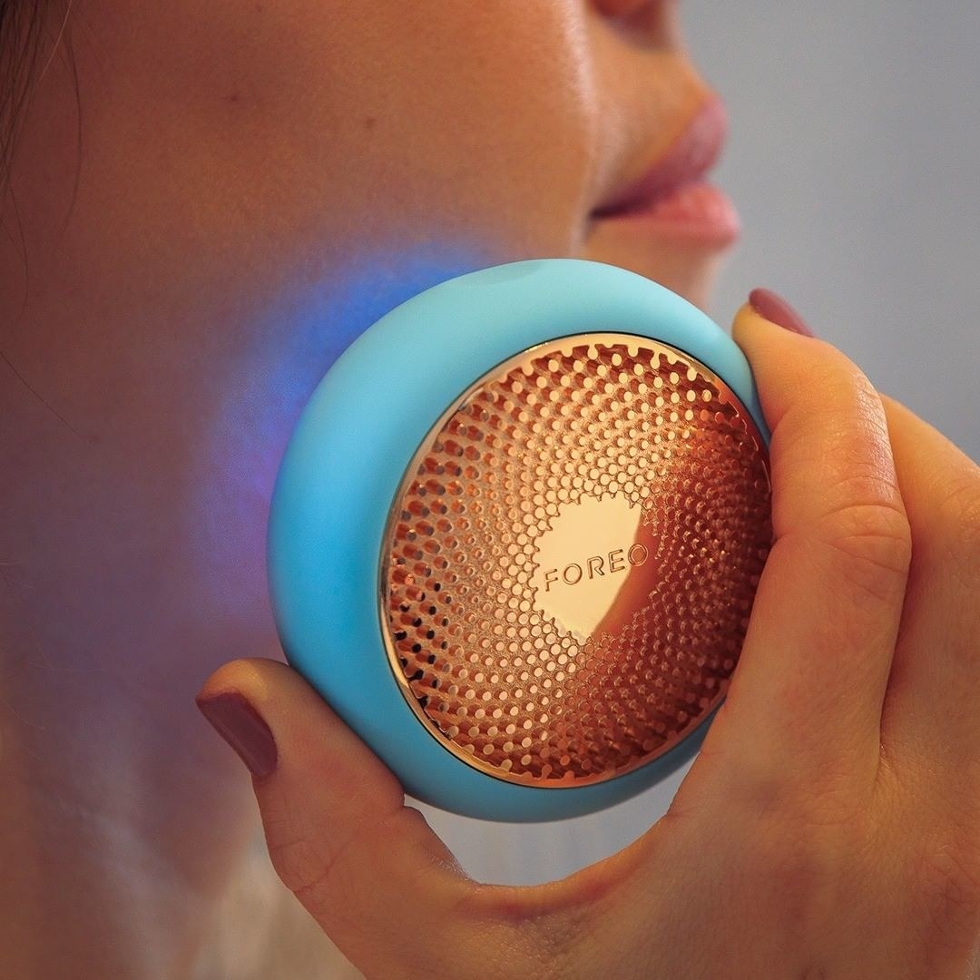 model holds round flat device that glows blue to face 