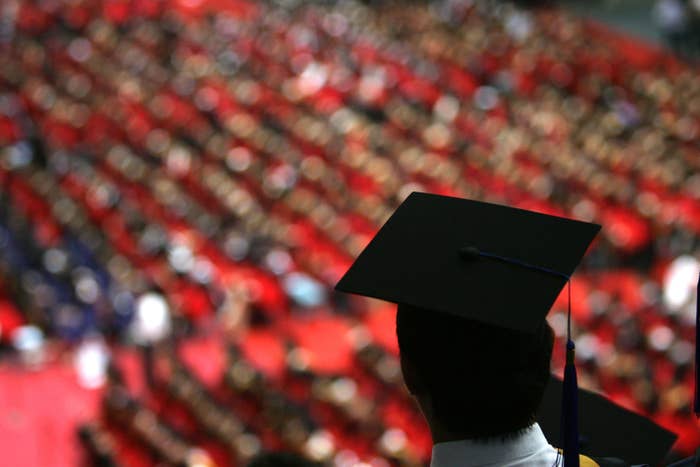A college graduate in a graduation cap looks out over a sea of fellow students.