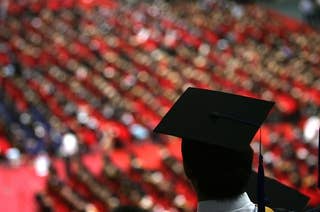 A college graduate in a  graduation cap looks out over a sea of fellow students