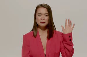 a woman wearing a blazer holds her hand up and looks relaxed 