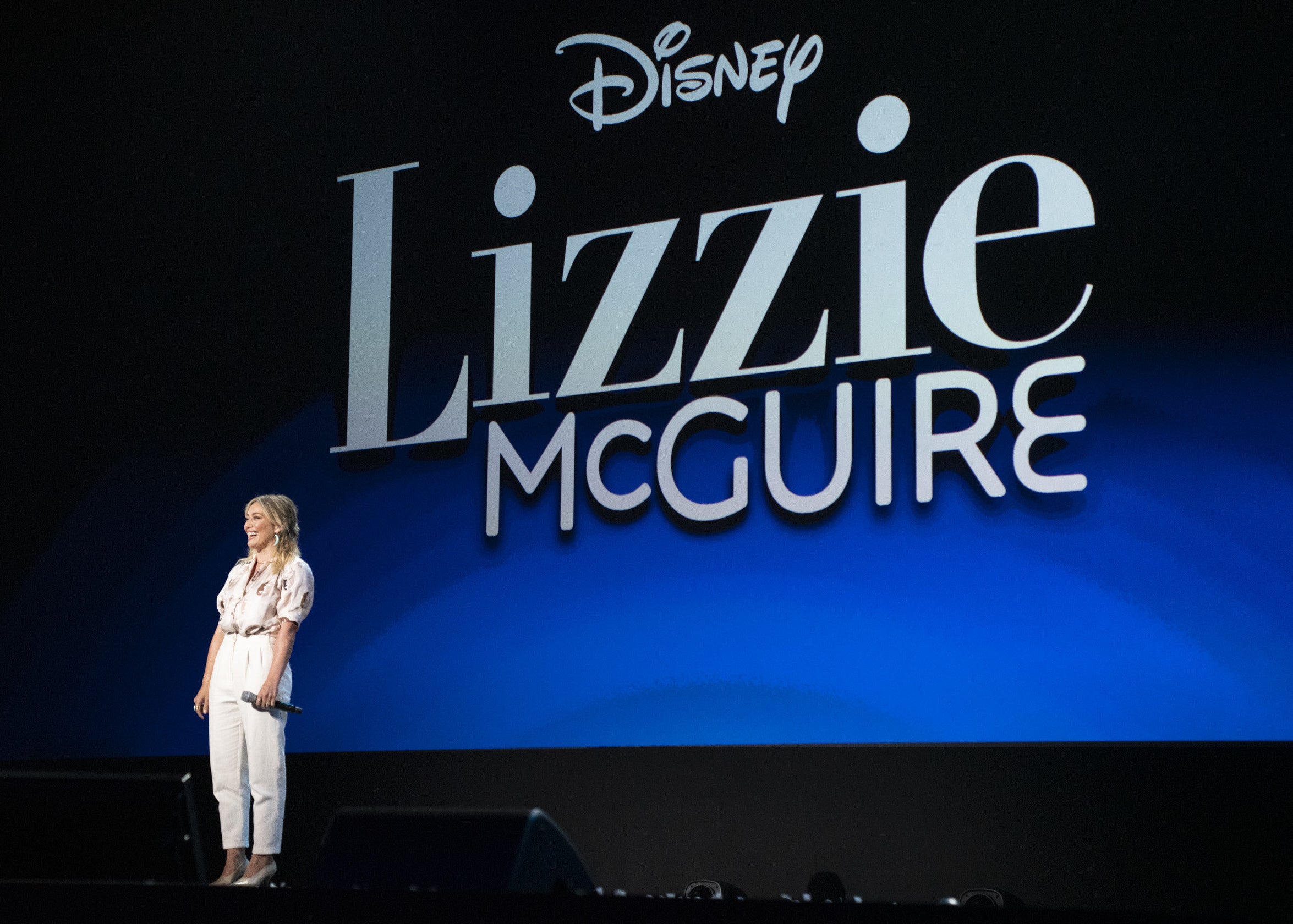 Hilary stands on stage in front of the "Lizzie McGuire" logo at a Disney event