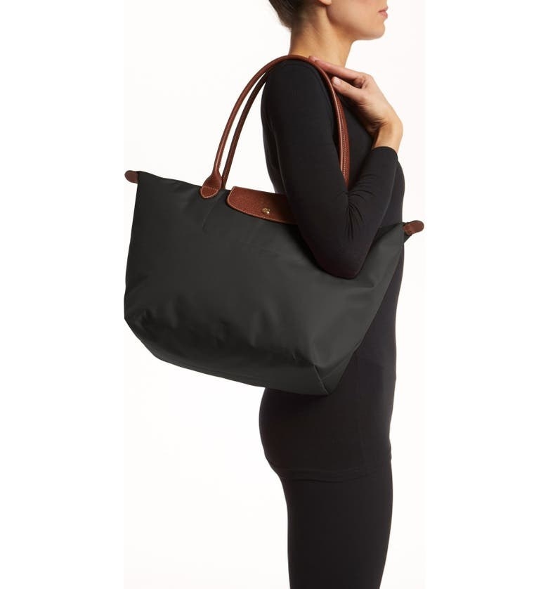woman carrying a black Longchamp nylon tote bag with brown leather trim