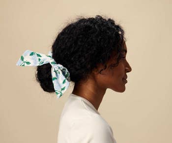 a model with a bow scrunchie around a low bun with a white and blue hydrangea print on it