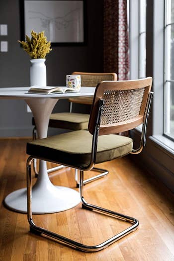 Two modern chairs at a dining table with a book, near a window in a cozy interior setup