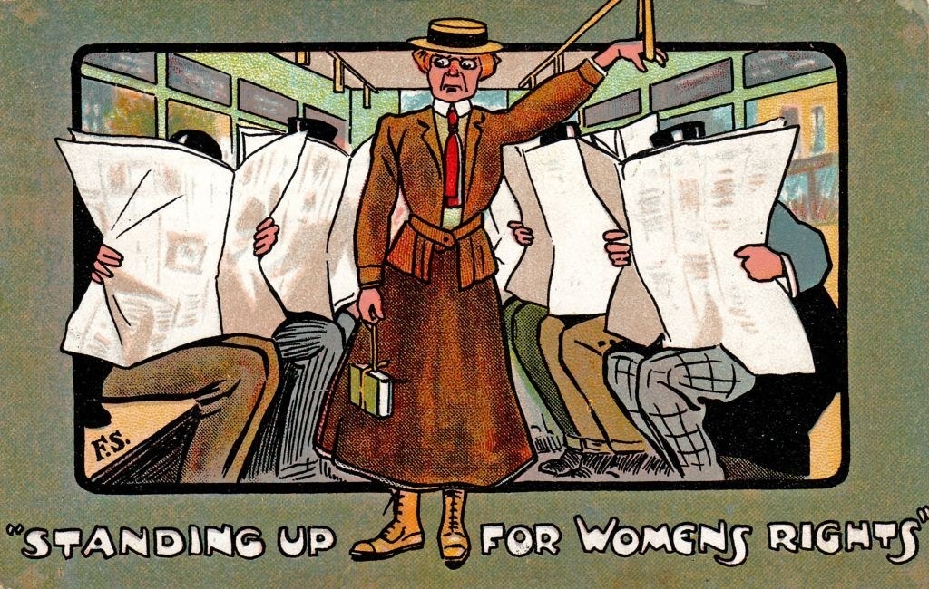 &quot;Standing up for womens rights&quot; written beneath a woman standing on the bus while man sit and read newspapers, ignoring her