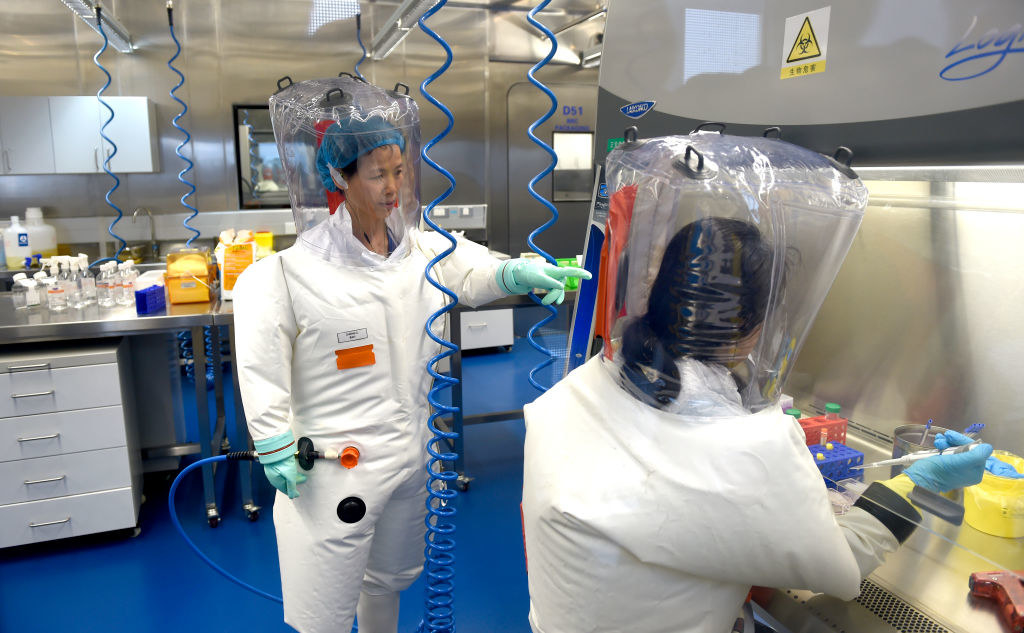 Two people wear full-body protective gear inside a lab