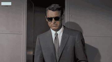 A gif of Cary Grant wearing sunglasses and looking for something
