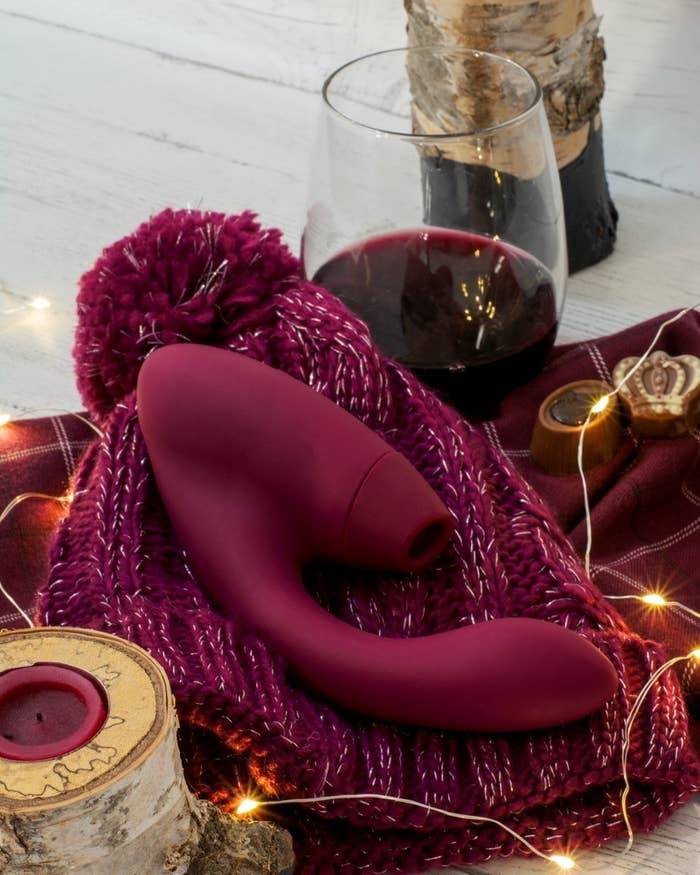 the womanizer duo atop a burgundy knit beanie hat surrounded by twinkle lights and a glass of red wine