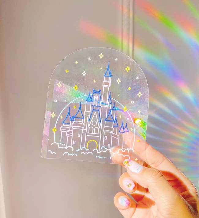 hand holds up a castle-shaped sun catcher casting small rainbows on a wall