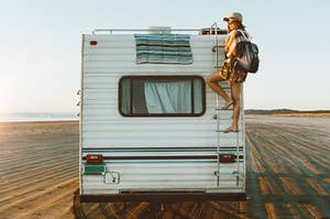 a girl standing on a ladder on the back of an RV driving on the beach