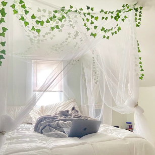 Reviewer while with decor and bedding, a white canopy, and faux vines on the bed 