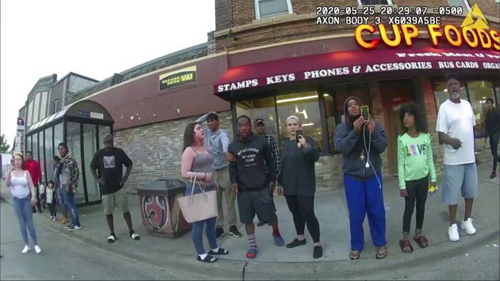 People standing on the sidewalk hold up cellphones in this still from a police body camera