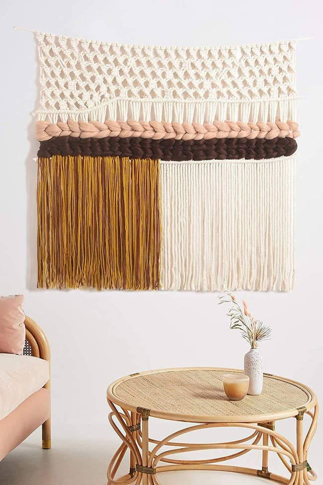 Multi-textured knit and tassel macrame wall hanging with sections of cream, yellow, brown, and pale pink yarn
