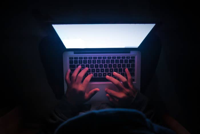 Ominous person using a laptop in a dark room