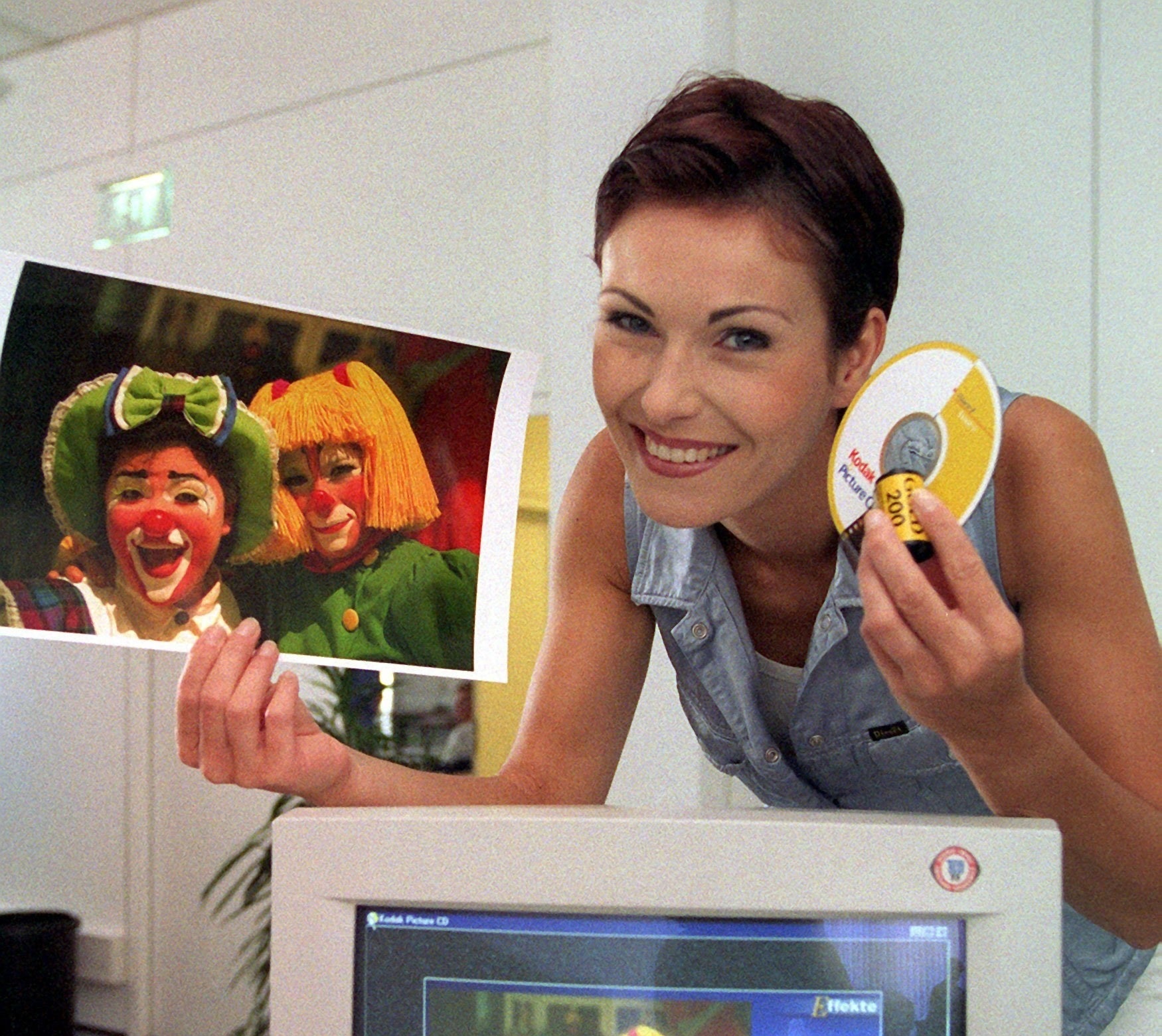 A woman holding a large photo of two female clowns in one hand and a photo CD and film in the other