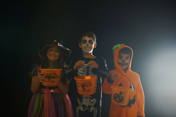 Stock photo of brothers and sister wearing halloween costumes holding trick-or-treat buckets
