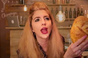 A blonde woman holds up a loaf of sourdough bread