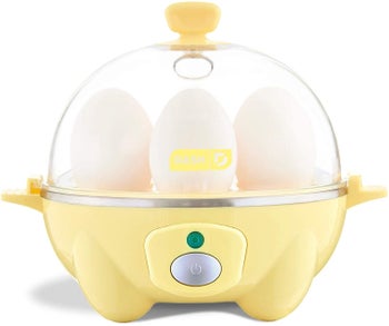 The egg cooker in pastel yellow, filled with eggs. It has a clear dome top and handles at the top and sides