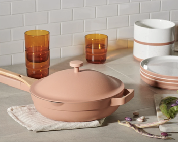 the pale peach colored always pan on top of a kitchen counter surrounded by amber cups and peach dishes