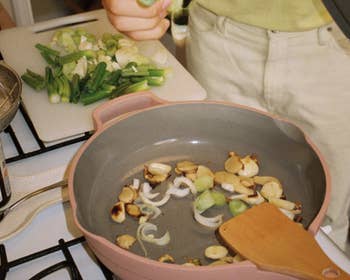 a model stands over the the spice colored always pan, sautéing mushrooms and onions on a stove