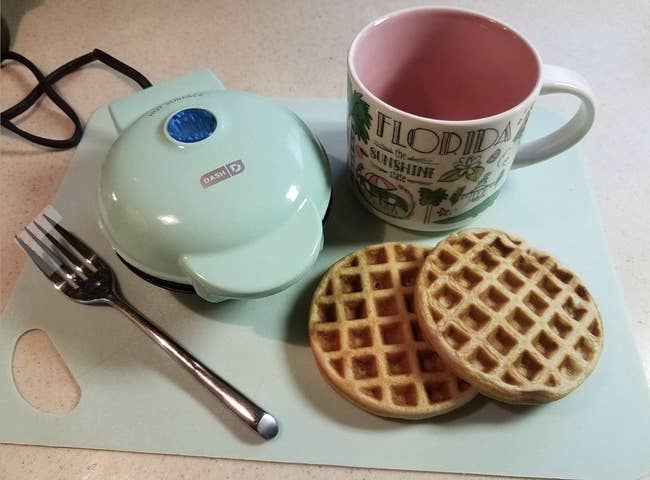 Reviewer's two cooked waffles next to small blue waffle-maker 