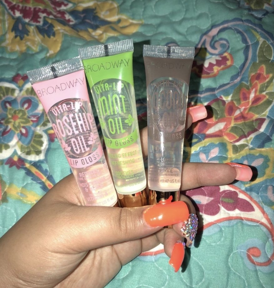 A person holding three lip glosses of different scents