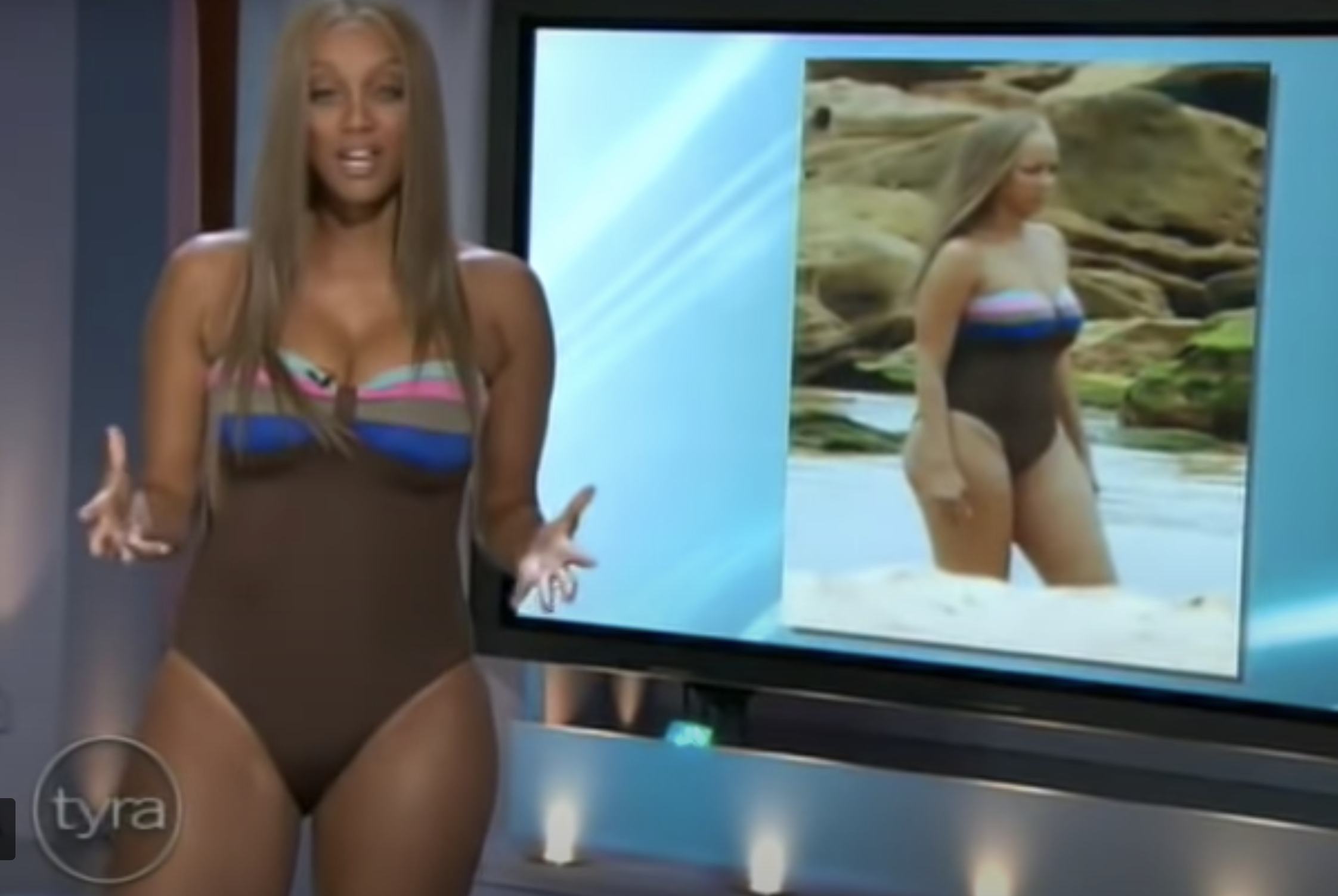 Tyra Banks wearing a bathing suit and talking on her show, with a picture of her in the same bathing suit at an unflattering angle on the screen behind her