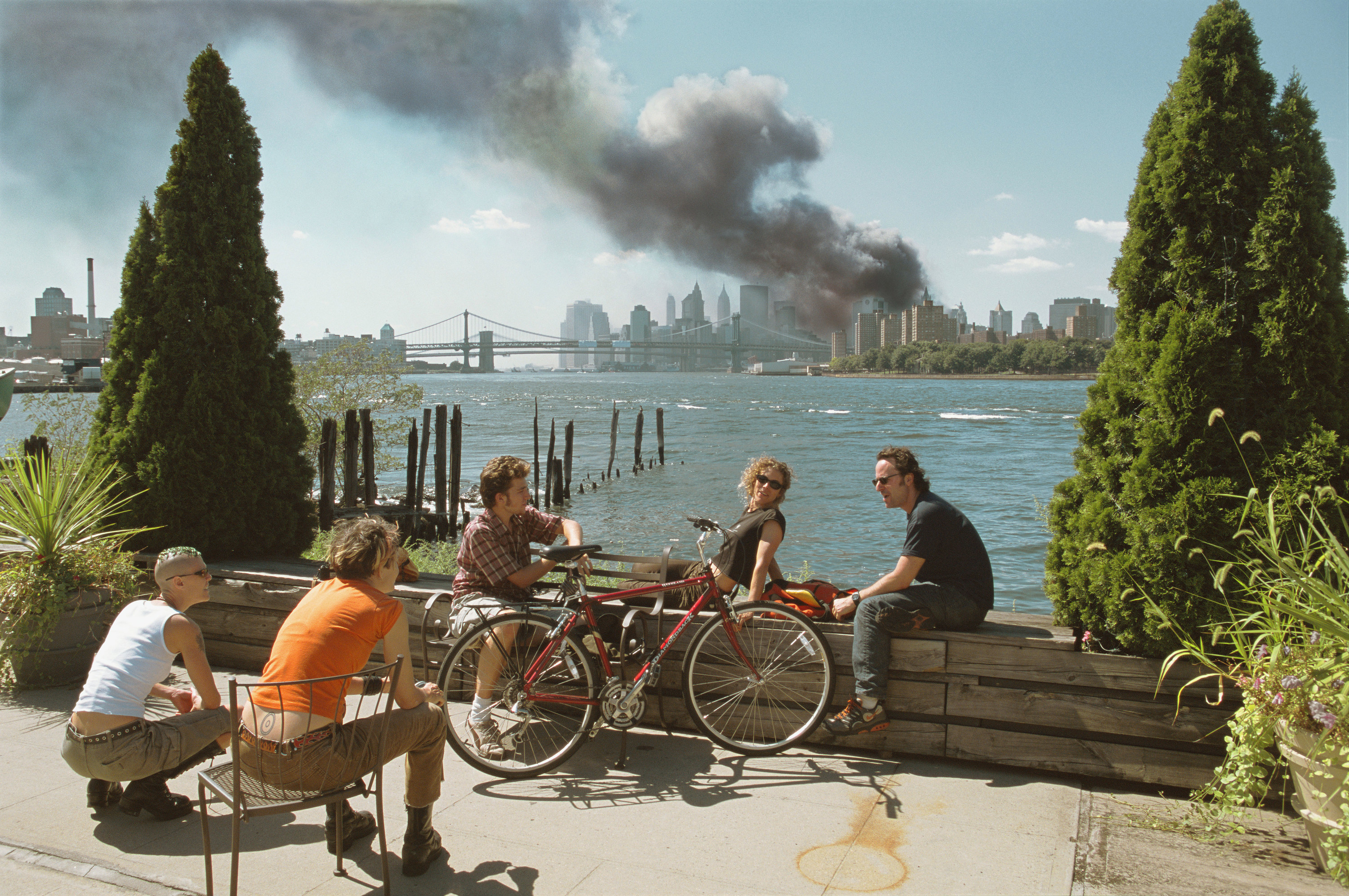 Young people relax during their lunch break along the East River while a huge plume of smoke rises from Lower Manhattan after the attack on the World Trade Center