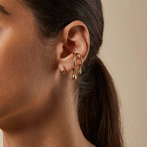 A person wearing a small hoop earring and two ear cuffs