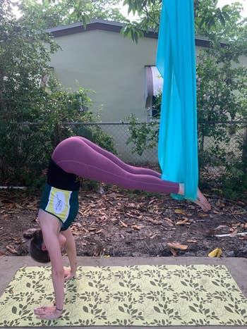reviewer stands in half handstand while using a blue aerial yoga hammock outdoors