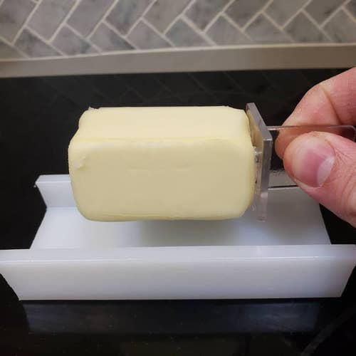 the white butter dish and a hand holding half a stick of butter by the clear holder