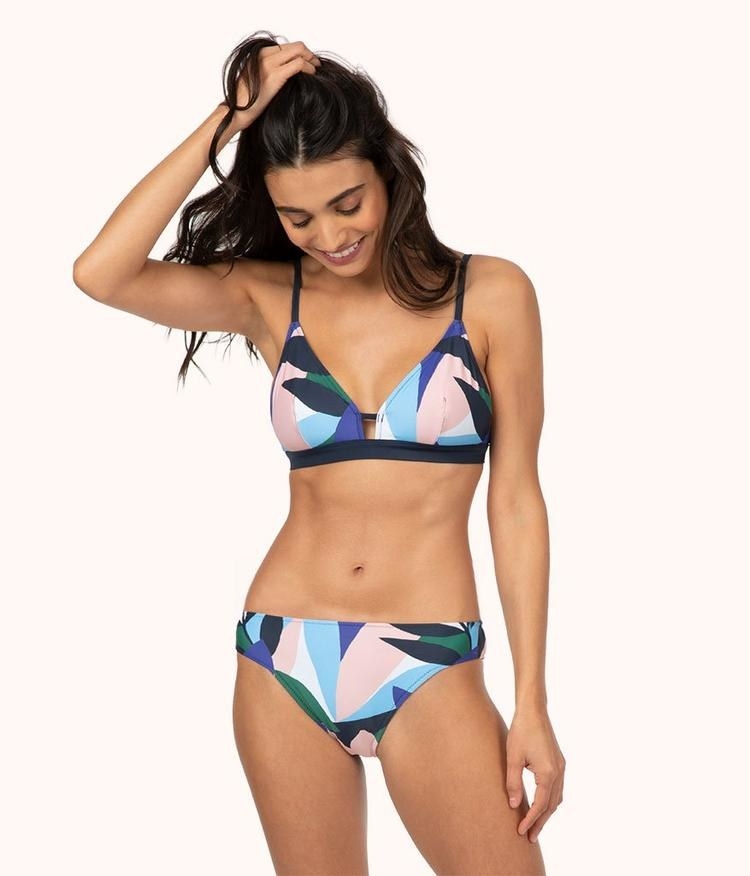 model wearing the bralette top and mid-rise bottoms with pink, blue, green, and navy graphic leaf print all over it