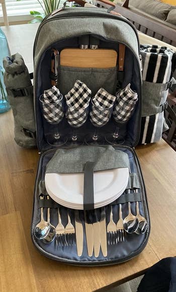 The open backpack showing the included wine glasses, plates, cutlery, and cutting board with a wine holder and picnic blanket strapped to each side 