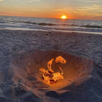 a reviewer photo of the portable fire pit sitting on the beach 