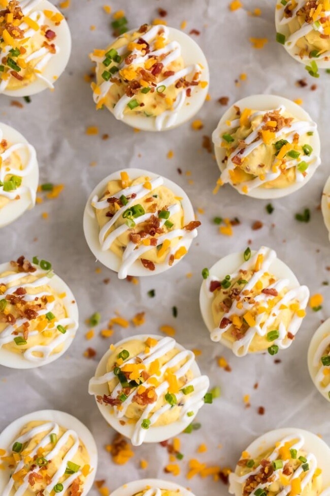 Deviled eggs topped with chives, bacon bits, and cheese.