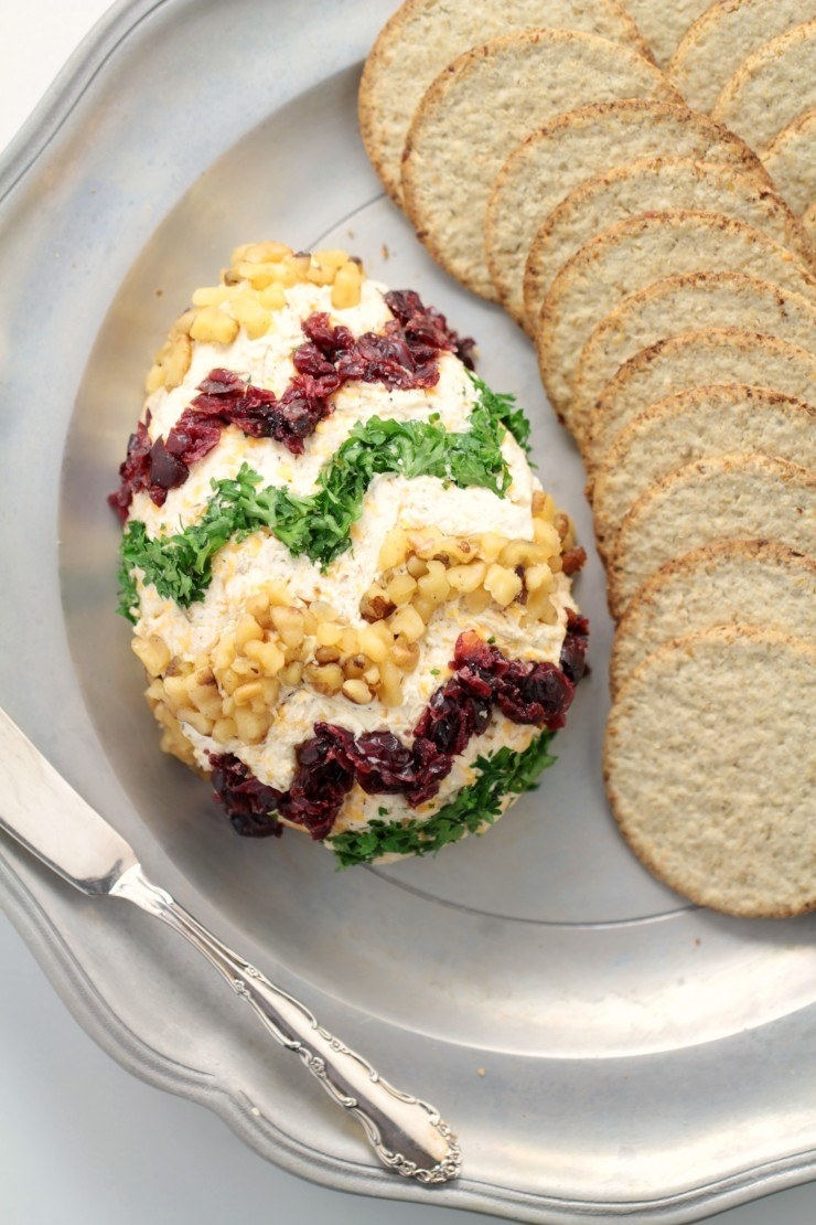 An Easter egg cheese ball garnished with herbs, cranberries, and nuts.