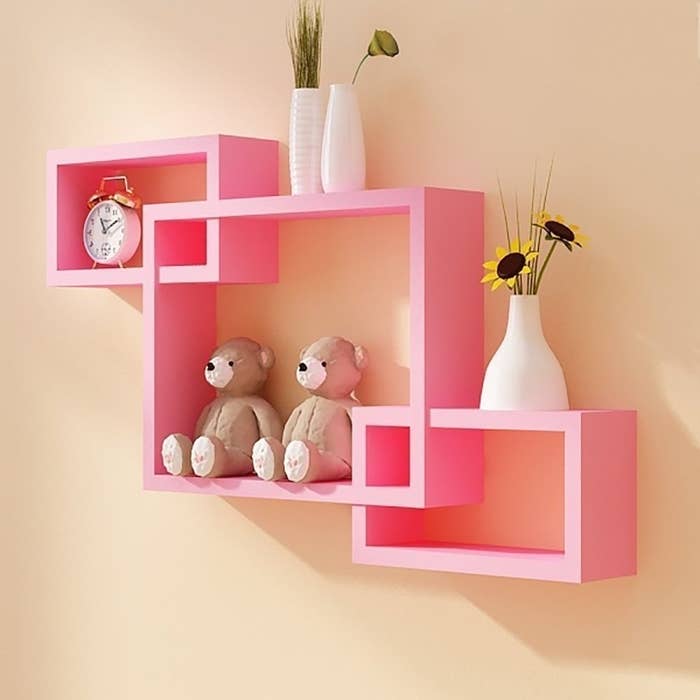 Pink shelves on a wall with items on them 