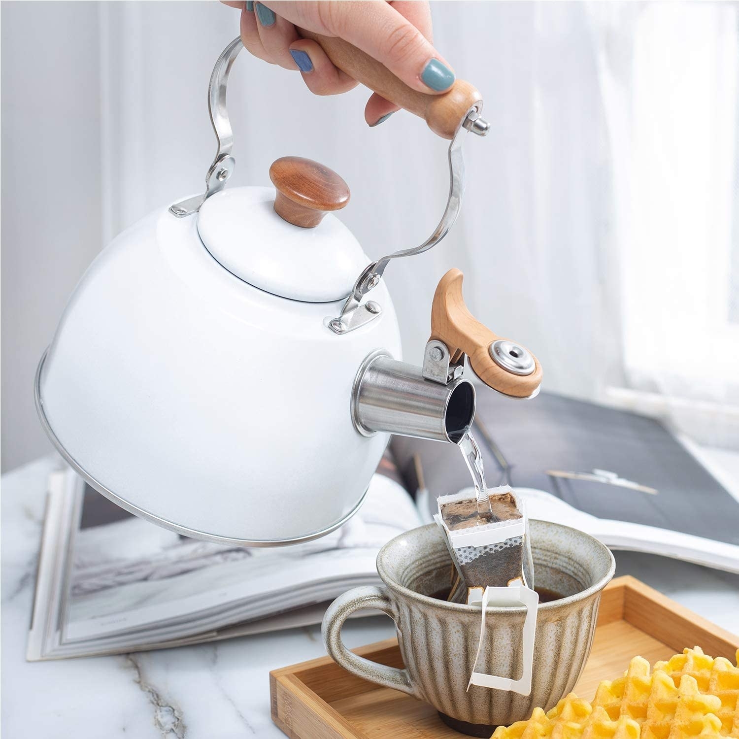 hand holds white, minimal-design tea kettle while pouring tea into cup