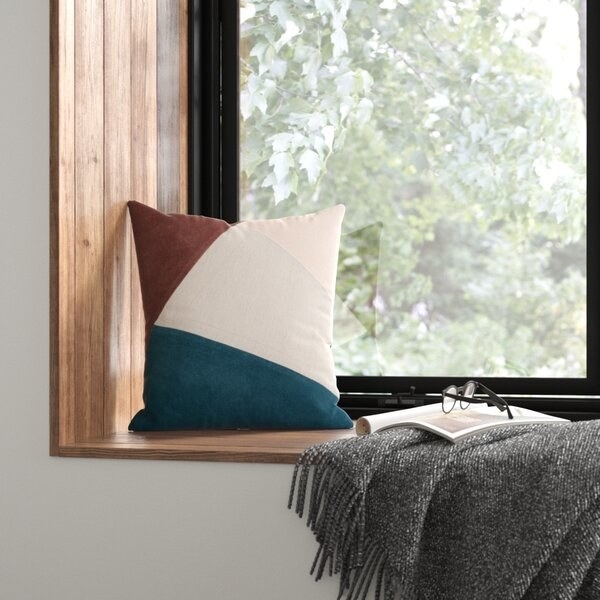 rust, navy blue, and white square pillow next to gray blanket on window nook