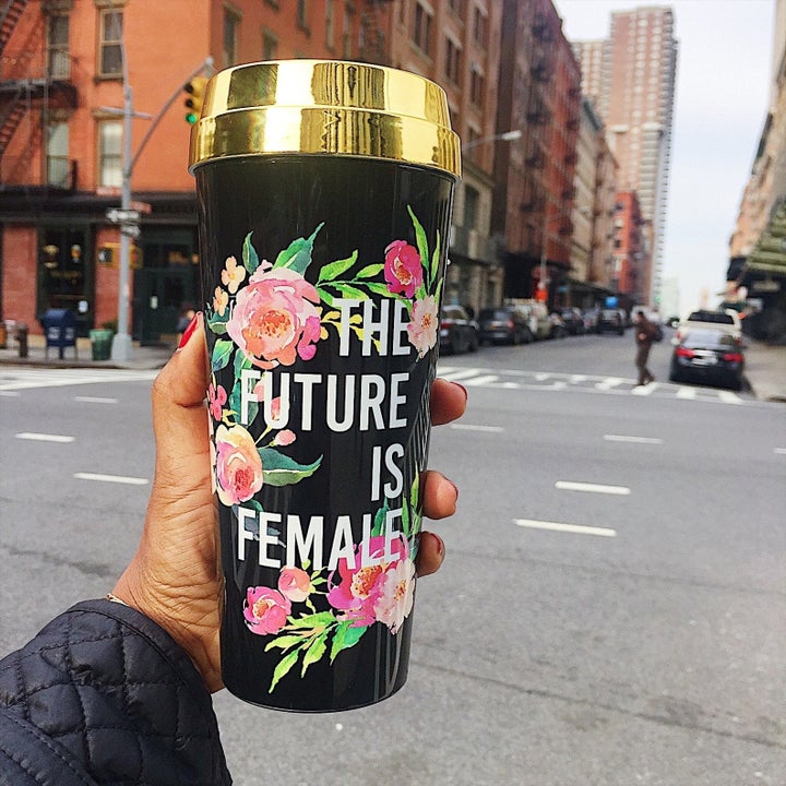 Model holding a black travel mug with gold lid and floral patter with white inscribed words "the future is female"