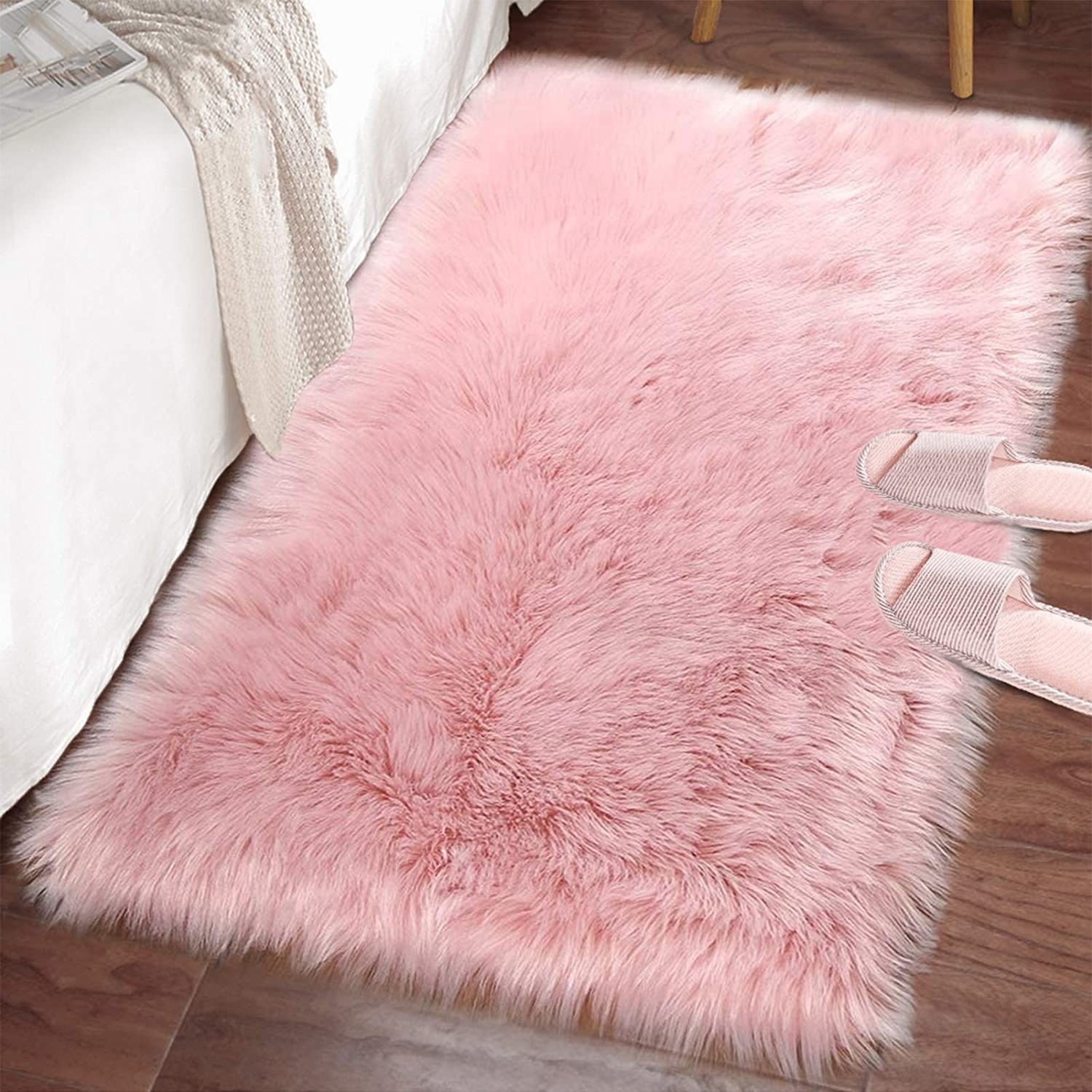 the fuzzy floor mat in pink on a wooden floor with slippers nearby