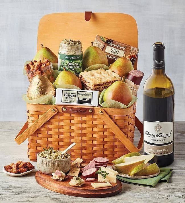 Classic picnic basket filled with fruit, nuts, and cheese with a wine bottle beside it 