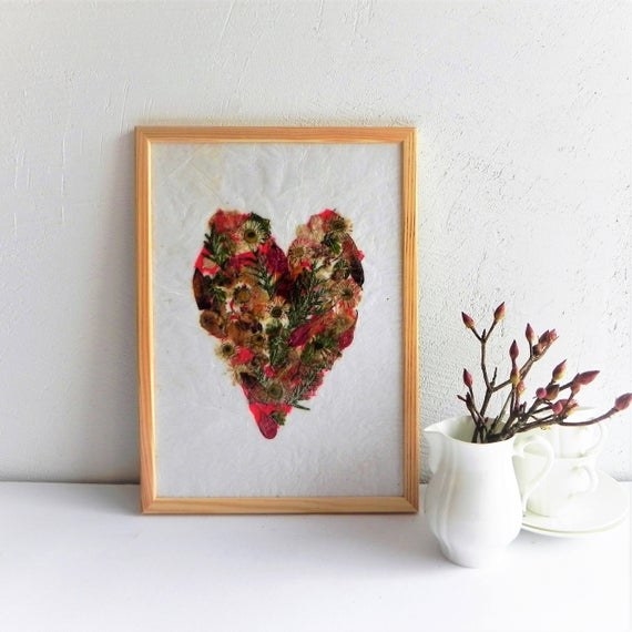 framed pressed pink and yellow flowers in the shape of a heart against a white wall