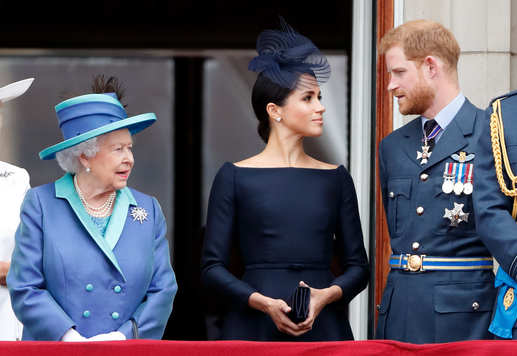 Meghan and Harry look at each other while standing next to the Queen at an event