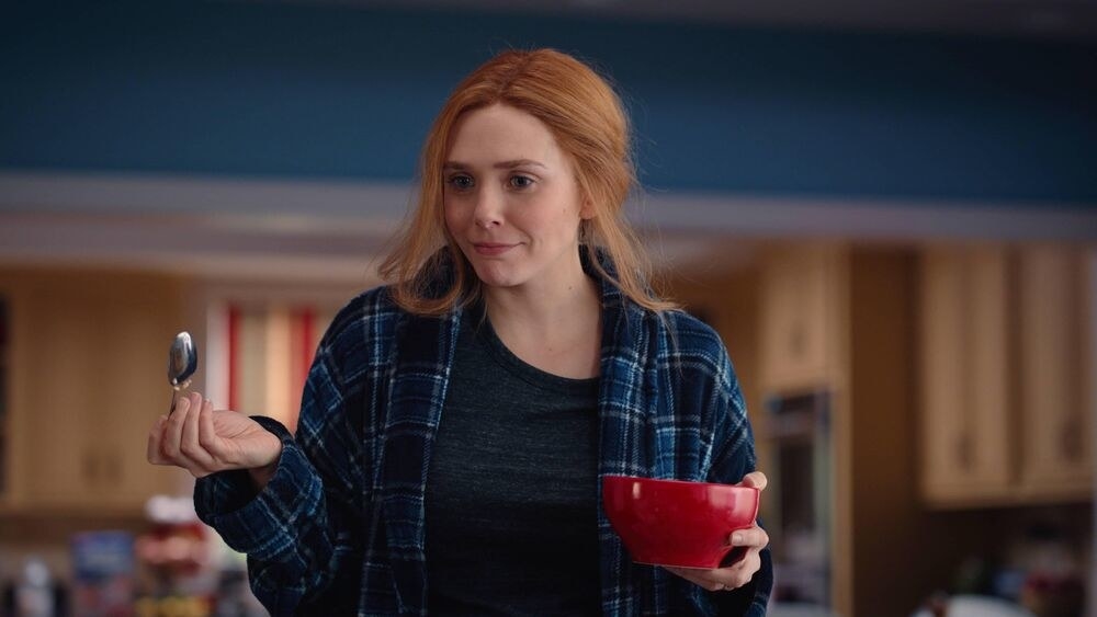 Wanda dressed in a blue flannel and gray shirt holds a red cereal bowl