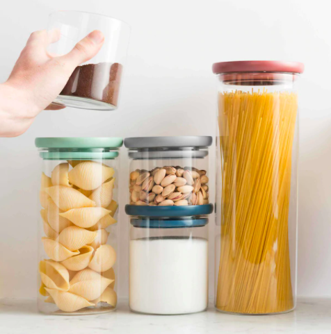 A person stacking a glass container full of coffee grounds next to other glass containers full of pantry ingredients