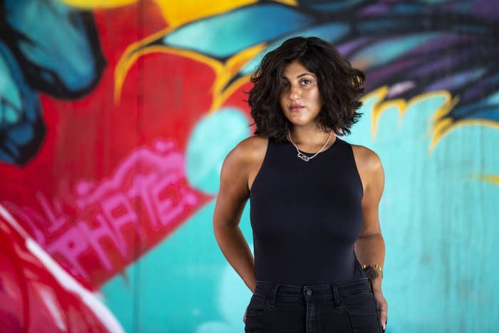 A woman stands in front of a colorful mural