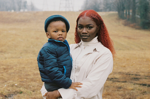 A woman holding her son close in a field of dry grass with electrical towers in the background